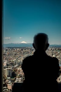 Silhouette of a person looking out of an office window over a city, (Tokyo) symbolising career change after 50 and the “window seat” idea.
